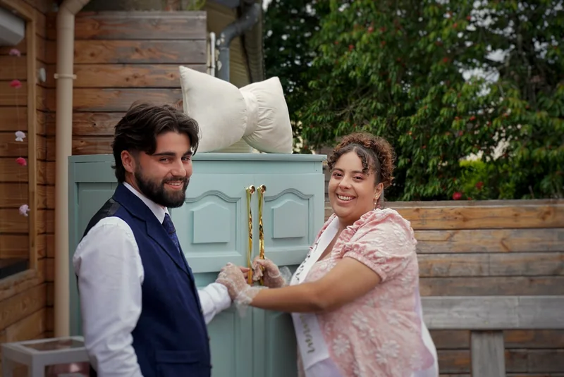 Un couple souriant côte à côte devant des portes bleues lors d’une fête