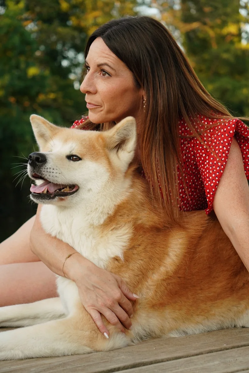 Une femme assise sur un ponton tient son chien contre elle