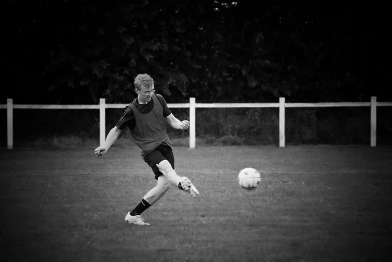 Un joueur frappe le ballon sur un terrain de football, en noir et blanc