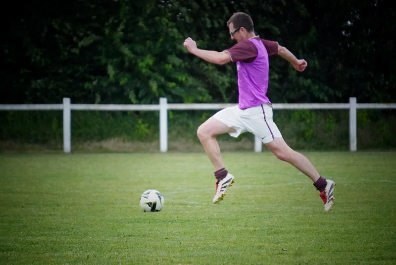 Un joueur de football saute au-dessus du terrain, le ballon devant lui