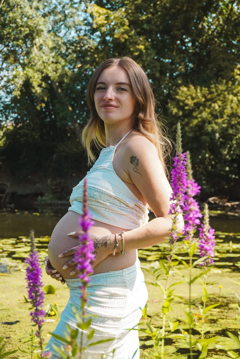 Une femme enceinte pose parmi les fleurs au bord de l’eau