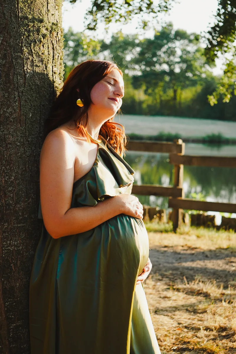 Une femme enceinte en robe verte s’appuie contre un arbre