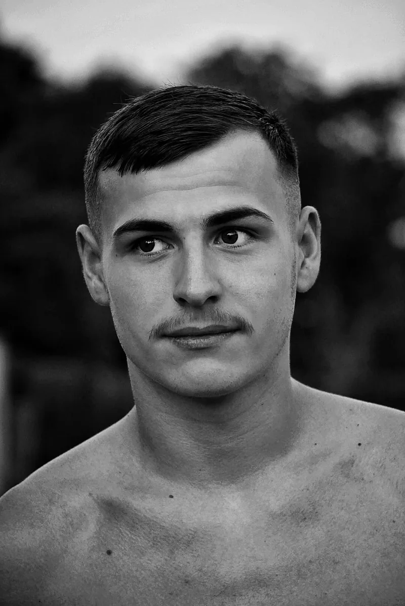Portrait de face d’un homme en noir et blanc, sur un fond arboré flou