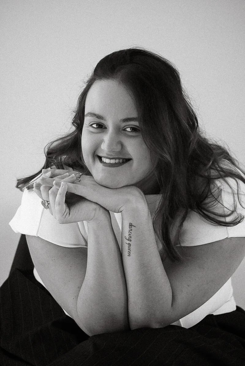 Portrait en noir et blanc d’une femme souriante, le menton posé sur les mains