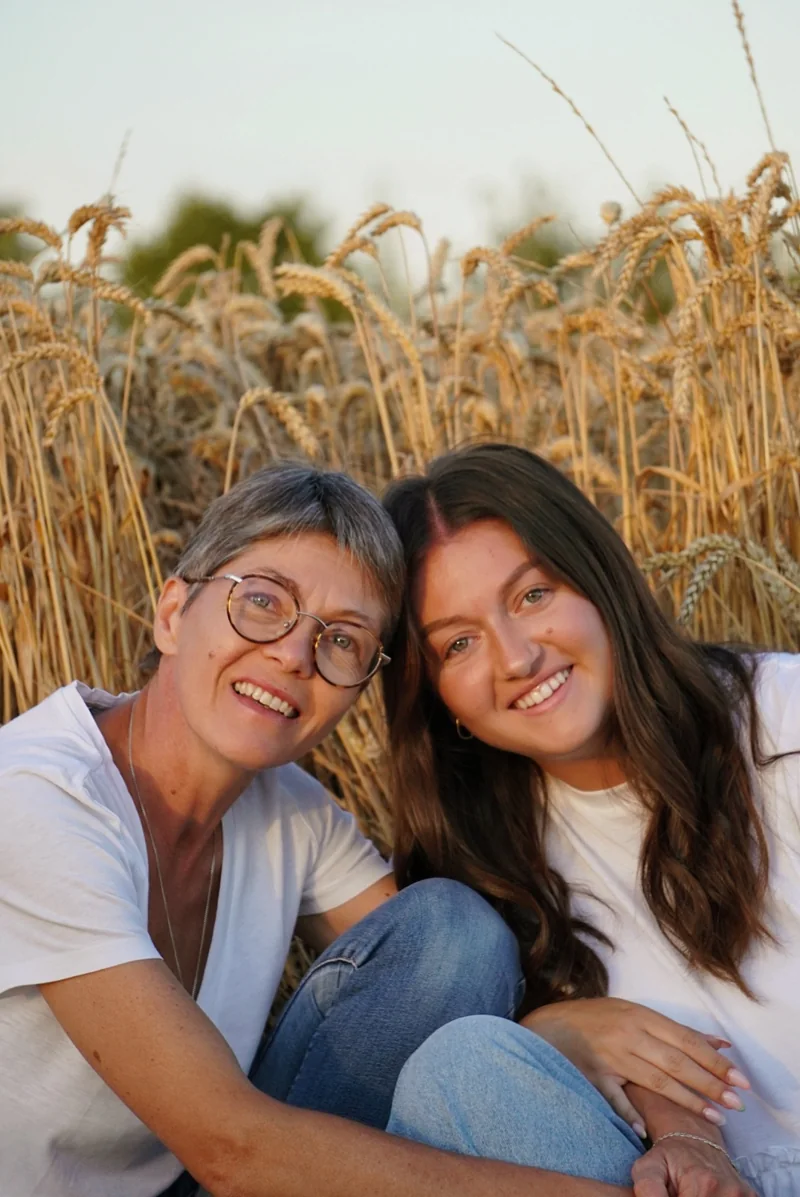 Deux femmes souriantes sont assises côte à côte devant les blés